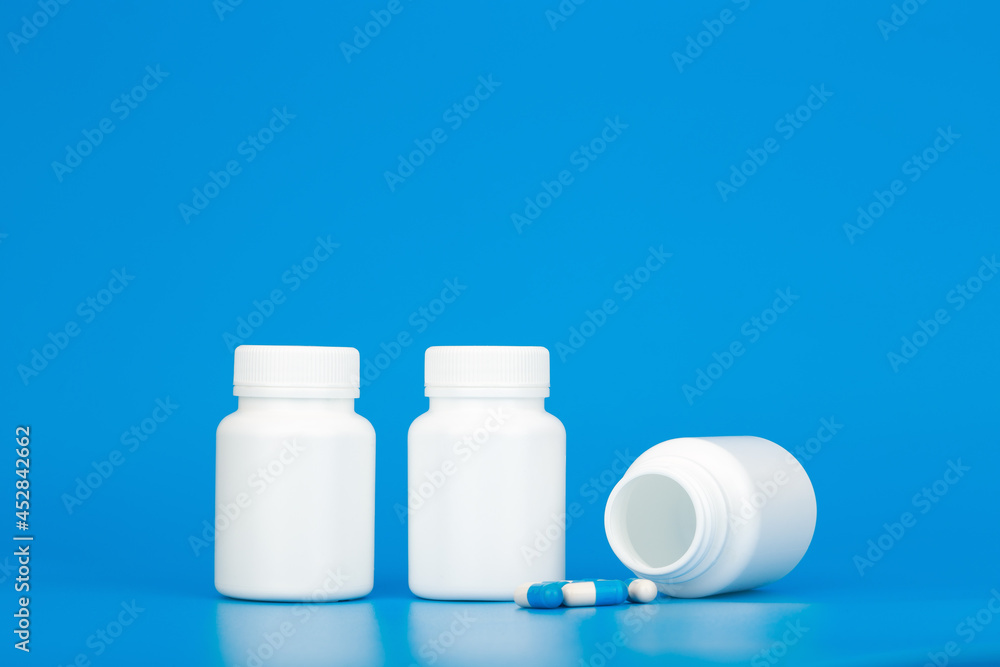 Minimal still life white medication bottles with pills against blue background with copy space. Concept of healthcare and medical treatment Minimal still life white medication bottles with pills against blue background with copy space. Concept of healthcare and medical treatment