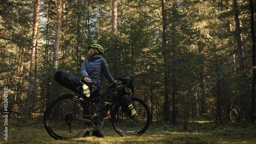 The woman travel on mixed terrain cycle touring with bike bikepacking outdoor. The traveler journey with bicycle bags. Stylish bikepacking  bike  sportswear in green black colors. Magic forest park.
