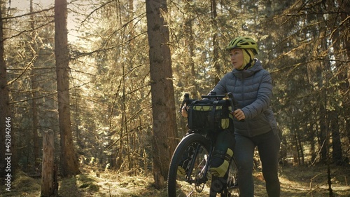 The woman travel on mixed terrain cycle touring with bike bikepacking outdoor. The traveler journey with bicycle bags. Stylish bikepacking, bike, sportswear in green black colors. Magic forest park. photo