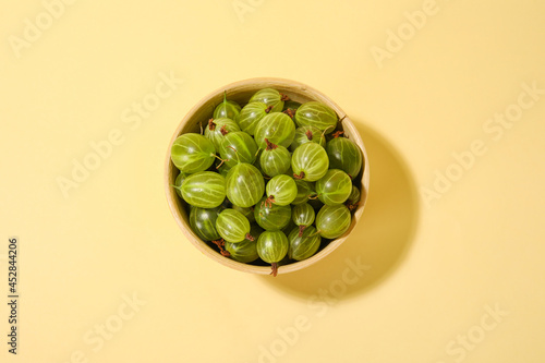 Bowl with fresh ripe gooseberry on color background