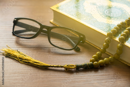 Selective focus of rosary beads, glasses and Quran on wooden background.