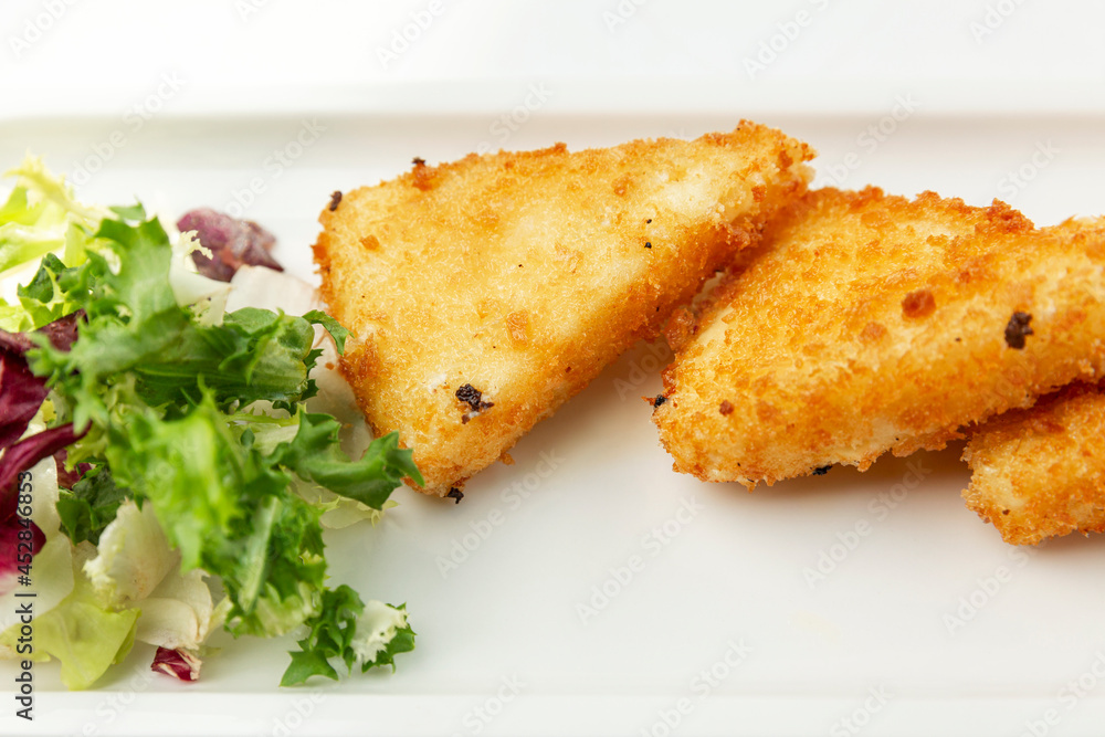 Pieces of fried cheese with lettuce on a white plate. Appetizing starter. Close-up. Pieces of fried cheese with lettuce on a white plate. Appetizing starter. Close-up.