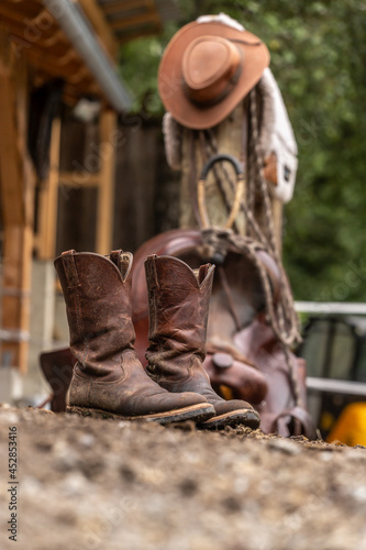 Ranch life scenery: muddy western boots in front of a western saddle. Cowboy boots. Muddy working boots