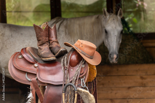 Equipment for western riding in front of a horse. A Western saddle, boots and a cowboy hat with a horse in the background. Western riding scenery photo