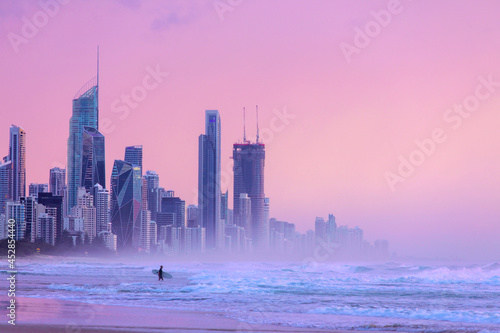 Sunlit skies over Surfers Paradise cityscape, with surfer going into the ocean