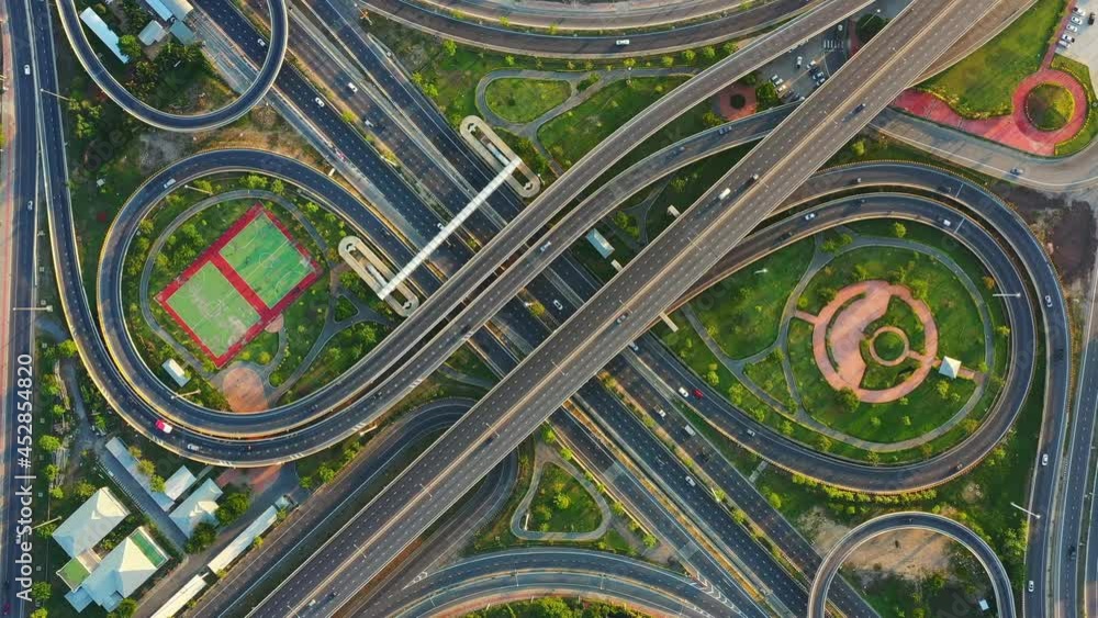 Time lapse of aerial view of highway junctions with roundabout. Bridge roads shape circle in structure of architecture and transportation concept. Top view. Urban city, Bangkok at sunset, Thailand. Time lapse of aerial view of highway junctions with roundabout. Bridge roads shape circle in structure of architecture and transportation concept. Top view. Urban city, Bangkok at sunset, Thailand.