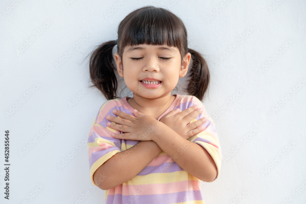 Close up of cute happy small girl isolated on white background hold hands at heart chest feel grateful, smiling little child with eyes closed pray thanking god high powers, faith concept Close up of cute happy small girl isolated on white background hold hands at heart chest feel grateful, smiling little child with eyes closed pray thanking god high powers, faith concept
