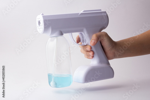 Hand holding a portable device for spraying on a white background. White alcohol spray for disinfection. Alcohol Fog Misting Nano Sprayer Gun.
