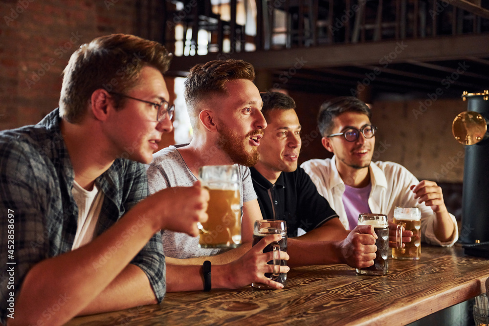 With beer in hands. People in casual clothes sitting in the pub With beer in hands. People in casual clothes sitting in the pub