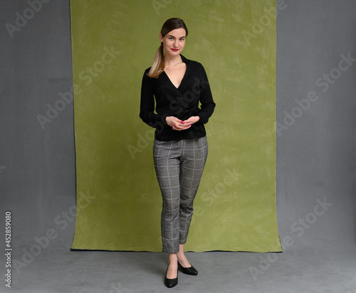 photo in full growth portrait of a young woman standing right in front of the camera in the studio on a gray-green background