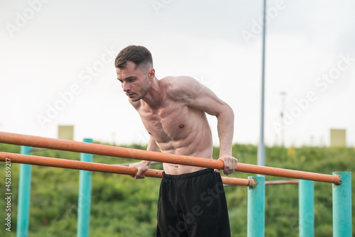 Young attractive Caucasian man doing push ups on the bars. Workout concept
