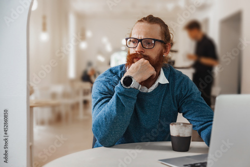 Pensive redhead man working on laptop in cafe