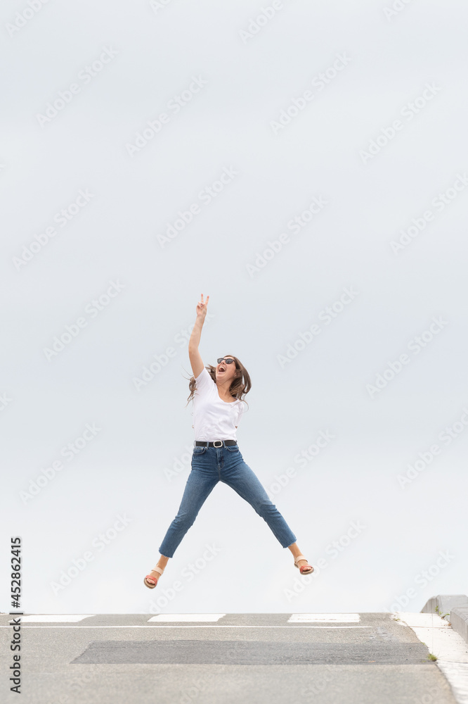 Happy casual dressed woman jumping on the pedestrian crossing of the road and celebrating victory. Happiness concept with copy space. Minimal composition with asphalt and sky Happy casual dressed woman jumping on the pedestrian crossing of the road and celebrating victory. Happiness concept with copy space. Minimal composition with asphalt and sky