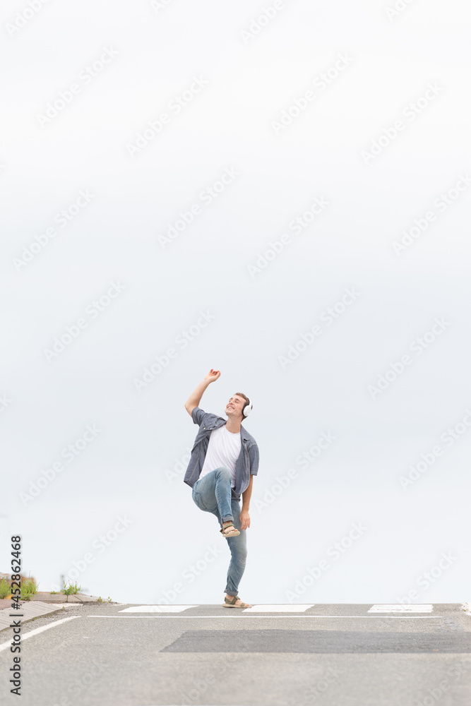 Young man listening to music and dancing in the middle of the road. Happiness and simplicity concept. Minimal composition with copy space.