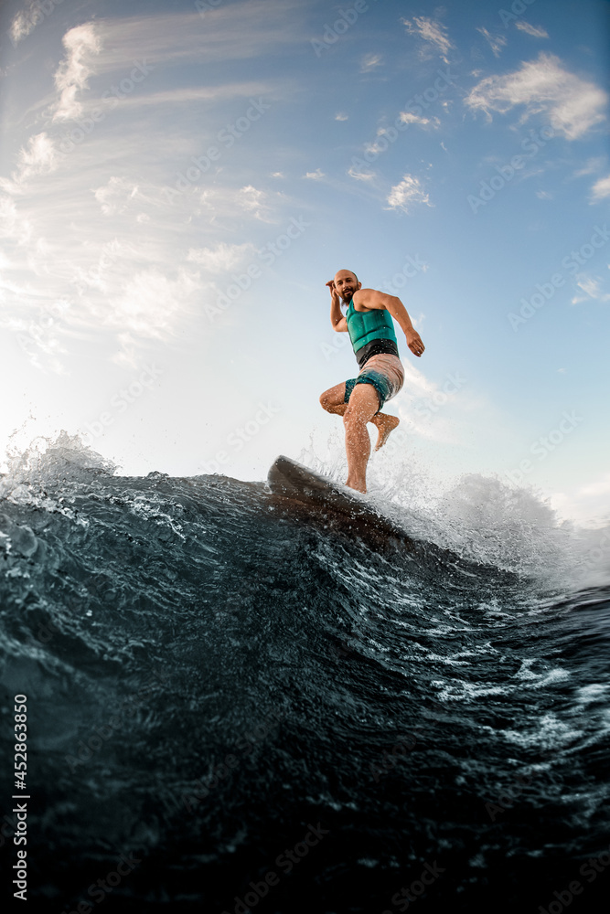 sportive man standing on one leg on a wakeboard and riding a wave