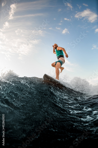 sportive man standing on one leg on a wakeboard and riding a wave