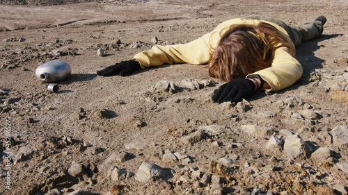 Girl exhausted from thirst lies in rocky wasteland with empty metal flask. Becoming weak hungry woman sprawled on ground. Drunk person is on sandy surface. Helplessness, early death in stone badlands photo