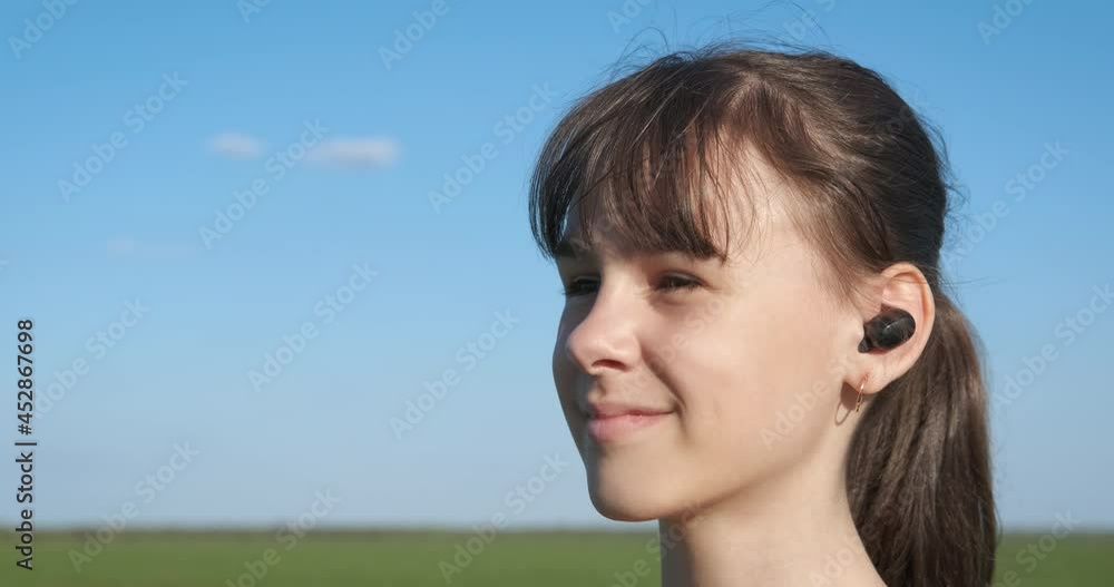 Music lover with wireless earbuds. A view of dancing child in wireless earbuds in the middle of green meadow in the country. Music lover with wireless earbuds. A view of dancing child in wireless earbuds in the middle of green meadow in the country.