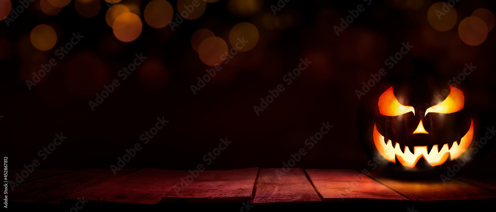 A scary halloween lantern with evil eyes and face on a rustic wood table with a spooky dark red background with faint light bokeh.