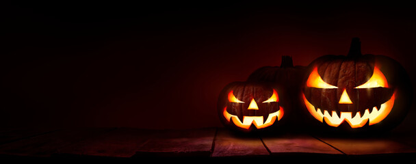 Three scary halloween lanterns with evil eyes and faces on a rustic wood table with a spooky dark red background.