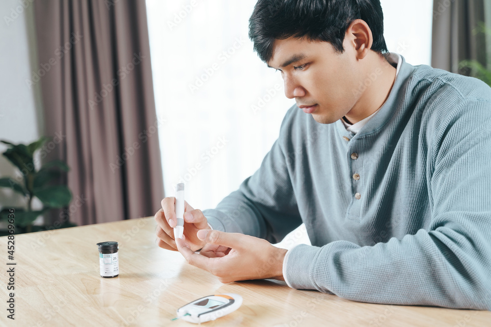 Asian man using lancet on finger for checking blood sugar level by Glucose meter, Healthcare and Medical, diabetes, glycemia concept Asian man using lancet on finger for checking blood sugar level by Glucose meter, Healthcare and Medical, diabetes, glycemia concept