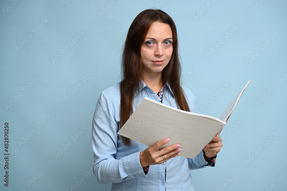 Portrait of a cute young girl in a blue shirt posing with a folder in her hands on a blue background Portrait of a cute young girl in a blue shirt posing with a folder in her hands on a blue background