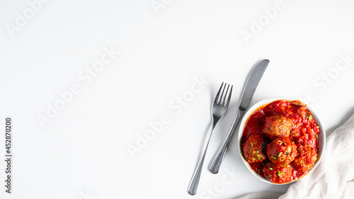 Top view of meatballs ball with tomato sauce and silver cutlery on whitebackground.Large iname for banner with copy space