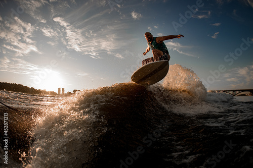 wakesurfer actively jumping over wave on the background of sky and sunset