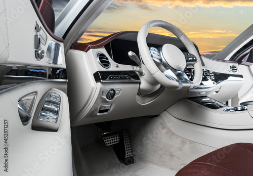 White luxury modern car Interior. Steering wheel and dashboard. Detail of modern car interior. Automatic gear stick. Leather seats with stitching in expensive car. Sunset sky background