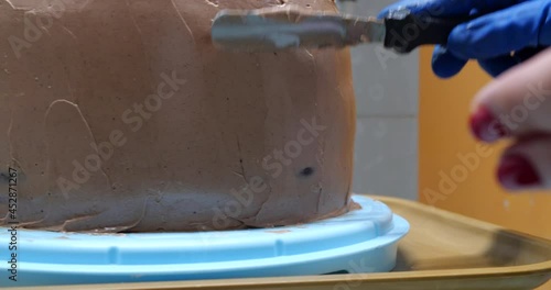 Confectioner woman is smearing cream on sides of cake using spatula, closeup view. culinary, baking and cooking food concept, home cooking