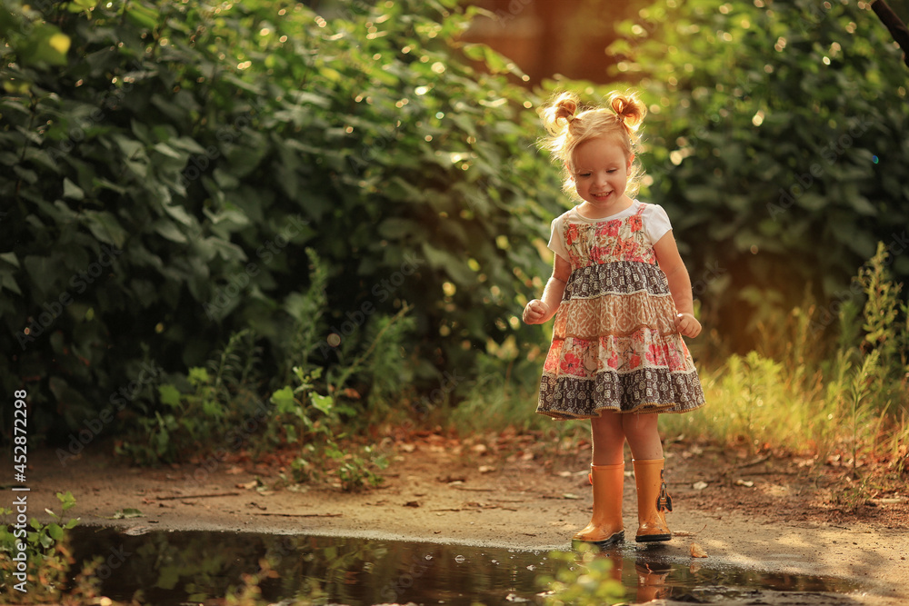Obraz premium little girl near the puddle in yellow rubber boots
