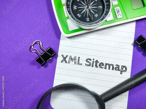 Business concept.Text XML Sitemap writing on notepaper with magnifying glass,compass,calculator and paper clips on purple background. photo