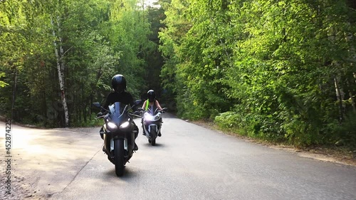 Motorbikes in the forest - two women riding motorcycles on the empty narrow road
