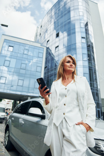 White car at background. Woman in formal wear standing outdoors in the city at daytime