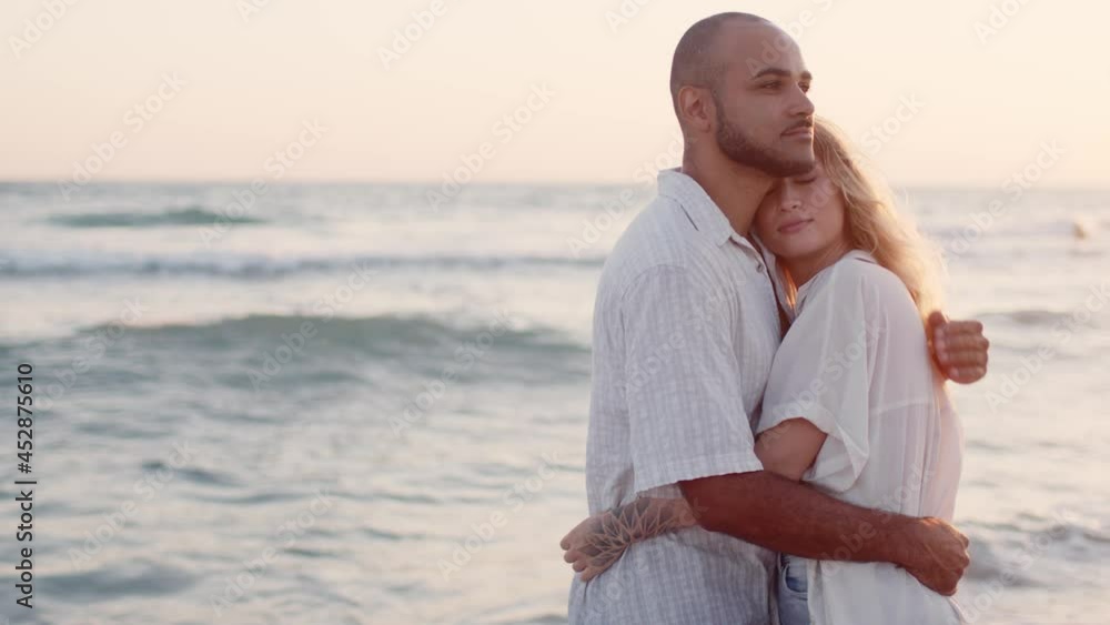 Young beautiful couple in love standing and hugging on beach by the sea Young beautiful couple in love standing and hugging on beach by the sea