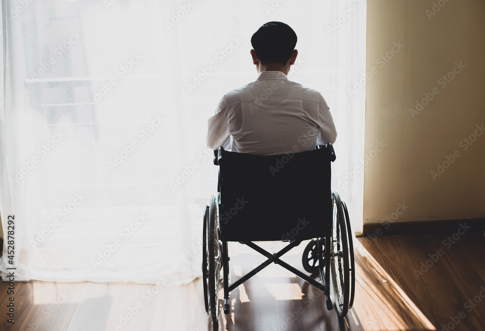 Back view of handicapped Man sitting on wheelchair in front of a large panoramic window in hospital,He is Lonely sad and deep in thoughts Back view of handicapped Man sitting on wheelchair in front of a large panoramic window in hospital,He is Lonely sad and deep in thoughts