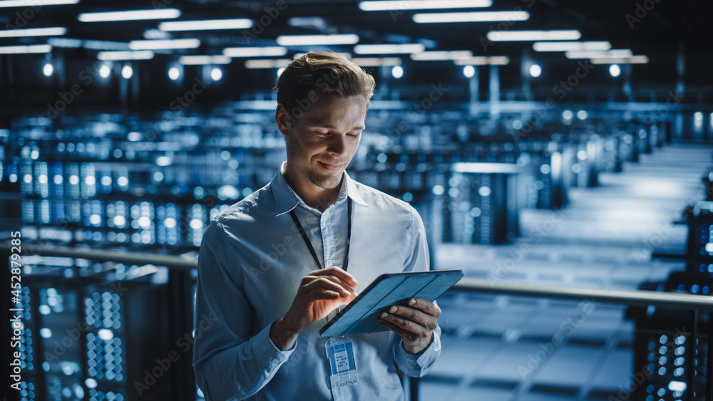 Fototapeta premium Portrait of Smiling IT Specialist Using Tablet Computer in Data Center. Big Server Farm Cloud Computing Facility with Male Maintenance Administrator Working. Cyber Security, e-Business.
