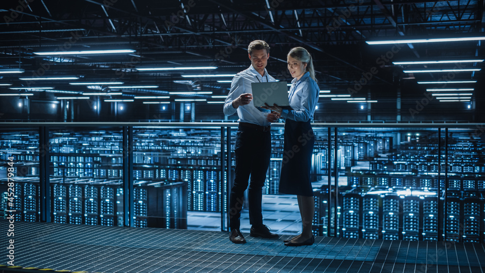 © Gorodenkoff - Data Center Female e-Business Enrepreneur and Male IT Specialist talk, Use Laptop. Two Information Technology Engineers on Bridge Overlooking Big Cloud Computing Server Farm. © Gorodenkoff - Data Center Female e-Business Enrepreneur and Male IT Specialist talk, Use Laptop. Two Information Technology Engineers on Bridge Overlooking Big Cloud Computing Server Farm.