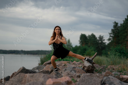Woman in black sport suit is doing fitness working out outside near beautiful river and stones