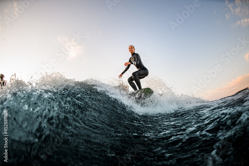 athletic female wakesurfer on the board rides down the river wave against the background of blue sky