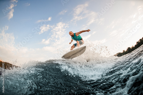 Man wakesurfer jumping on wake board down the river waves. Male athlete on wakesurf training.