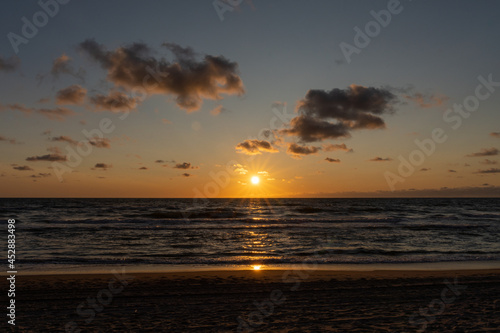 colorful beach sunset with the sun dropping into the ocean under an expressive sky