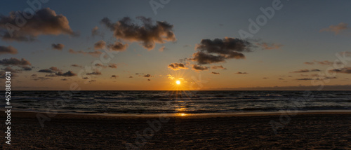 panorama of a colorful beach sunset with the sun dropping into the ocean under an expressive sky