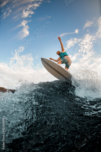 bottom view of man in a turquoise vest balancing on wakeboard on splashing wave of the river