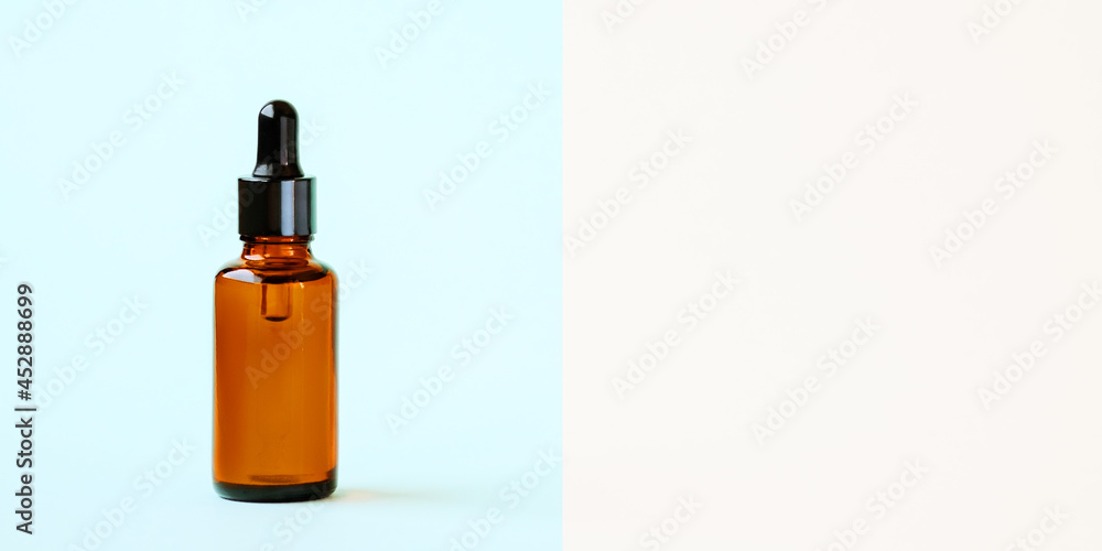 A mock-up of an empty glass dropper bottle made of brown amber glass on blue background. Skin care serum, banner or template. The concept of a natural cosmetic product.Copyspace. A mock-up of an empty glass dropper bottle made of brown amber glass on blue background. Skin care serum, banner or template. The concept of a natural cosmetic product.Copyspace.