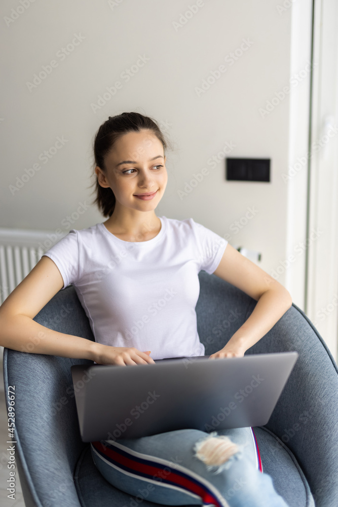 Young woman sitting on chair with laptop at home Young woman sitting on chair with laptop at home
