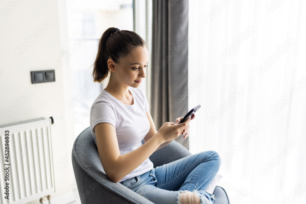 Young woman sit in chair use smartphone wear casual style clothes in house indoors Young woman sit in chair use smartphone wear casual style clothes in house indoors