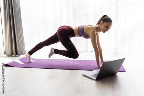Fitness woman training yoga, watching online videos on laptop in the living room at home