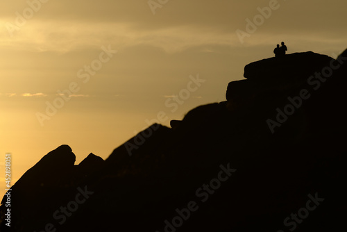 A couple stand silhouetted against a sunset atop stanage edge