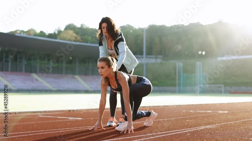 Caucasian Athlete ready to start. Young female runner with personal trainer preparing for blasting off in mist on sports track of stadium, training before competition. Sportswoman. Cardio exercises photo